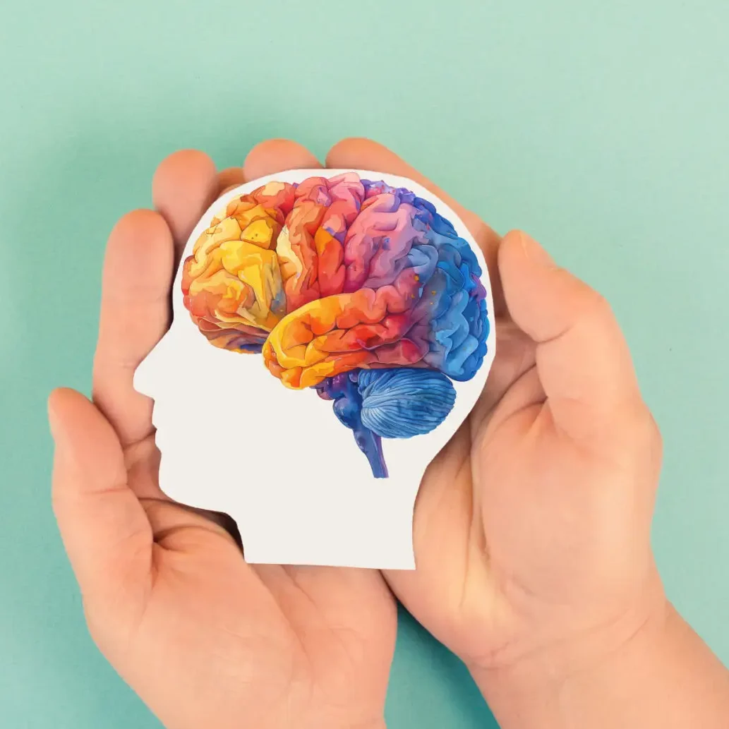 Hands holding head silhouette with colorful brain